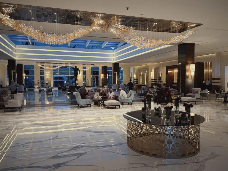 Innenansicht einer weitläufigen und luxuriös gestalteten Hotel-Lobby mit Marmorbodenfliesen und einem großen, dekorativen Kronleuchter.