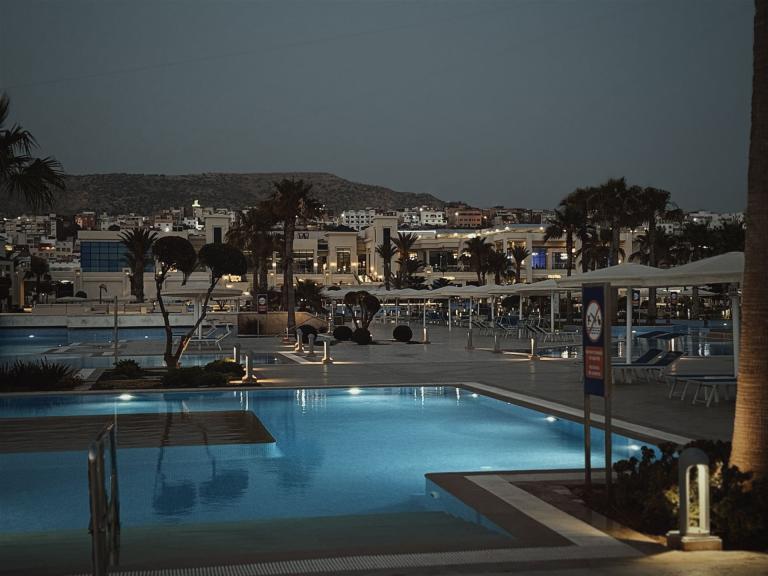 Ein großer Poolkomplex eines Resorts bei Dämmerung, mit Hotels und Palmen im Hintergrund.