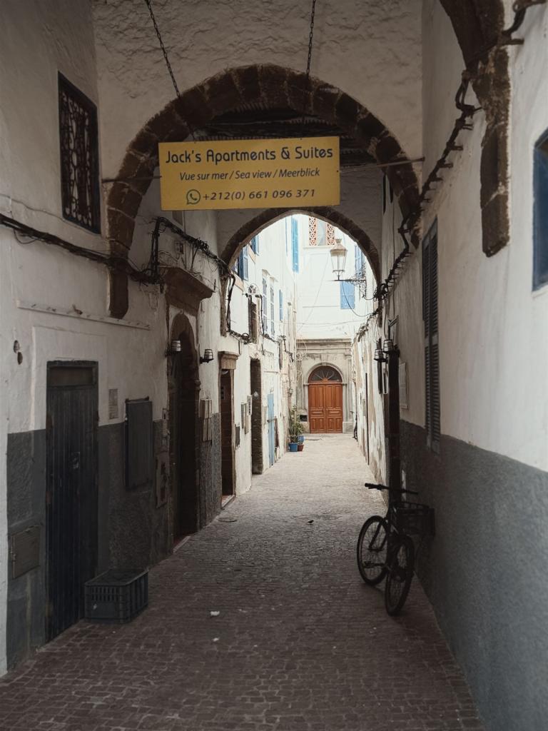 Eine enge, gepflasterte Gasse, die unter einem großen gemauerten Torbogen in einer historischen Altstadt hindurchführt.