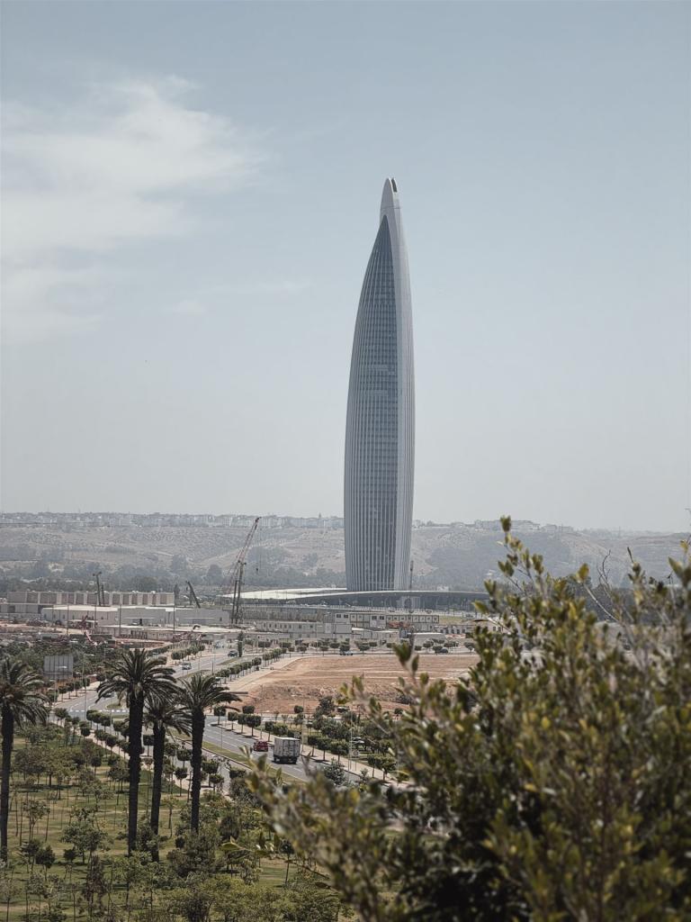 Ein hoher, schlanker Wolkenkratzer dominiert die Skyline und ist von grüner Vegetation im Vordergrund umrahmt.