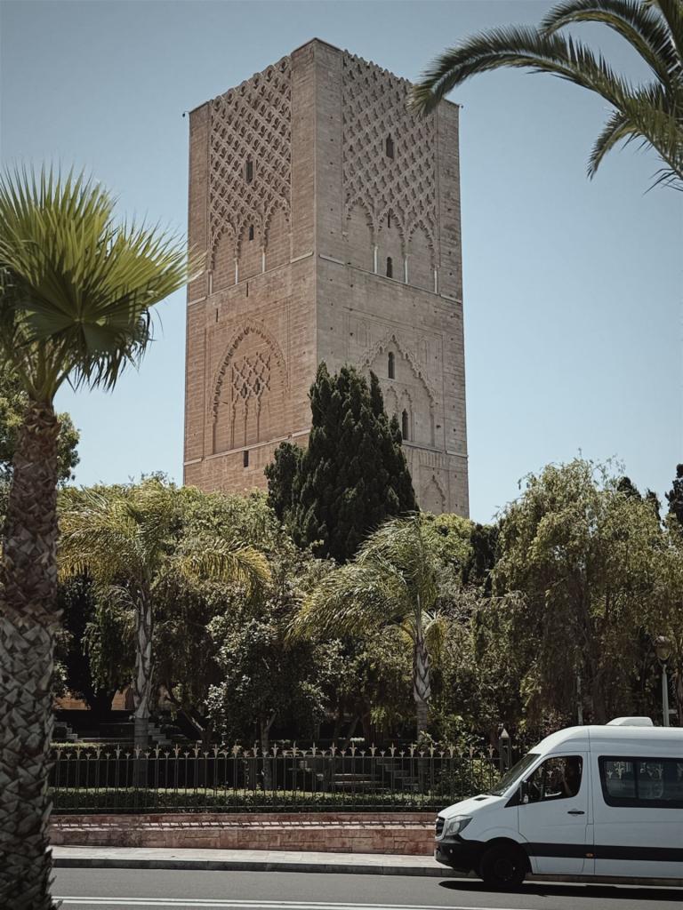 Ein massiver Backsteinturm mit kunstvollen Verzierungen überdacht von Bäumen und einem klaren blauen Himmel