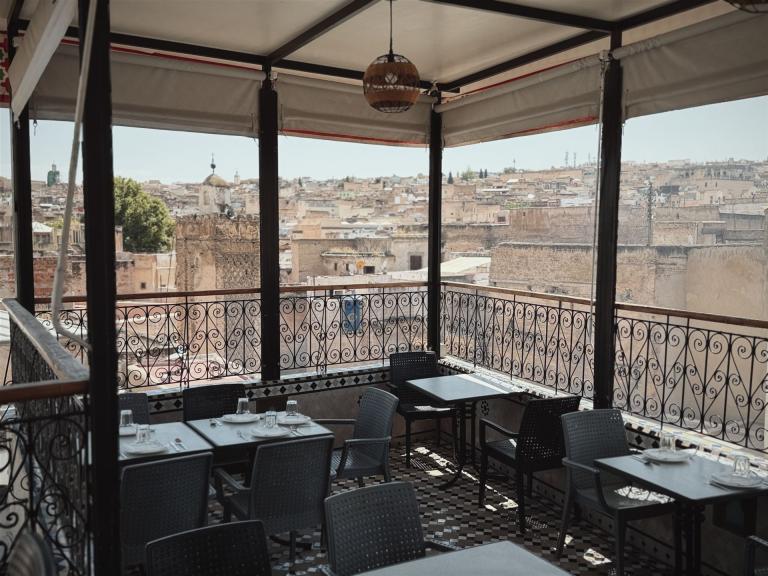 Restaurantterrasse mit Blick auf eine historische Stadtkulisse, bestehend aus Tischen und Stühlen.