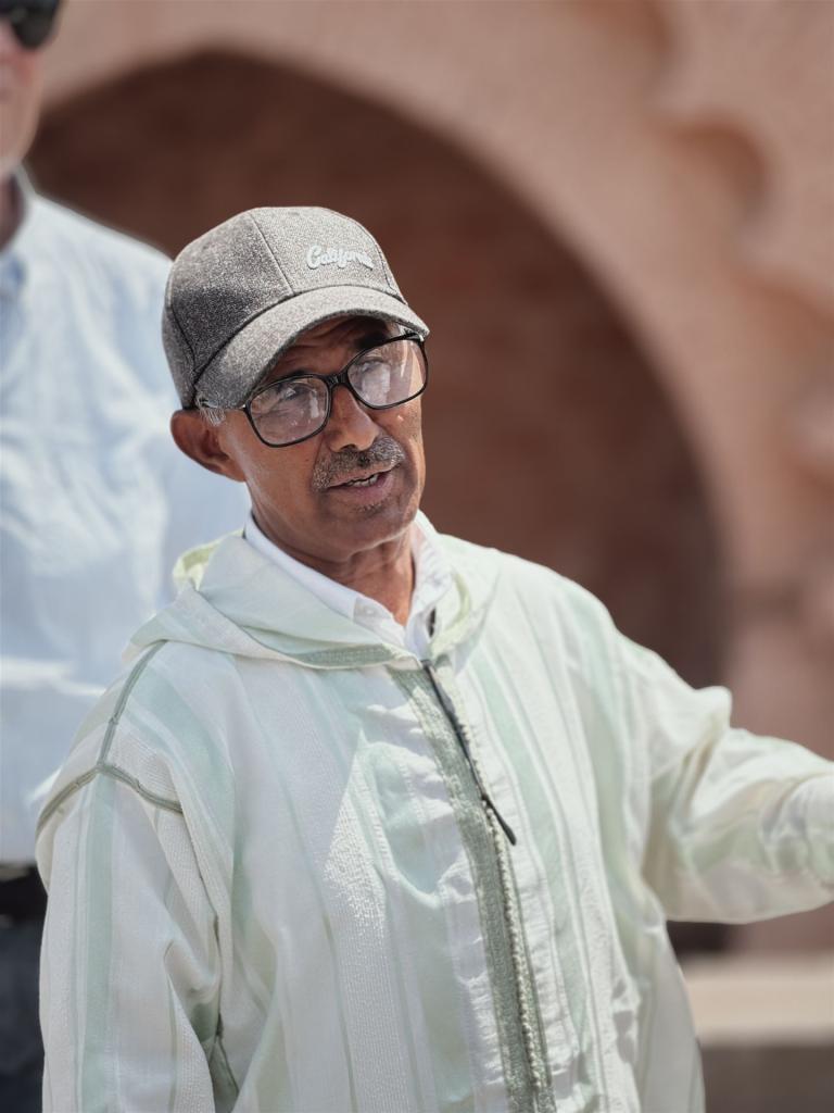 Porträt eines älteren Mannes mit Brille und Baseballkappe in einer hellgrünen Jacke.